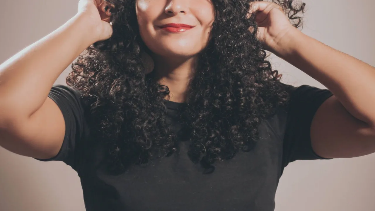 Pessoa com cabelo cacheado ajustando os fios, representando aplicação e definição