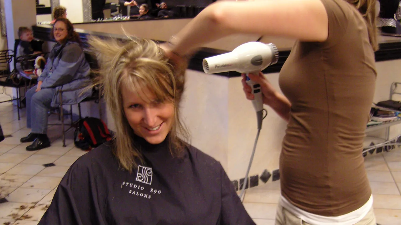 Profissional secando o cabelo de uma cliente com um secador em um salão.