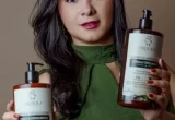 Pessoa segurando dois produtos de cuidados capilares diante de fundo neutro