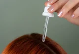 Pessoa aplicando sérum com conta-gotas sobre o cabelo ruivo