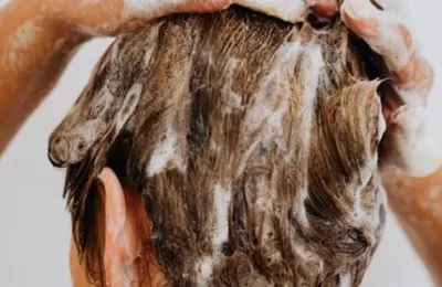 Pessoa massageia o cabelo coberto de shampoo durante a lavagem