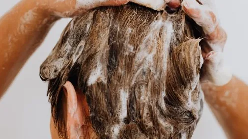 Pessoa massageia o cabelo coberto de shampoo durante a lavagem