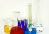 Vidrarias de laboratório com soluções coloridas, imagem contextual sobre pesquisa de ingredientes cosméticos.