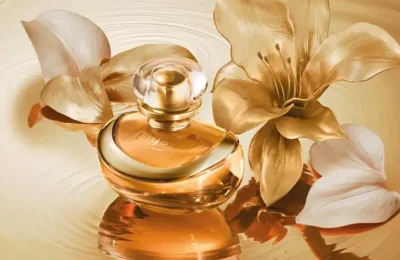 Frasco dourado do perfume Lily L’Or Elixir entre flores de lírio