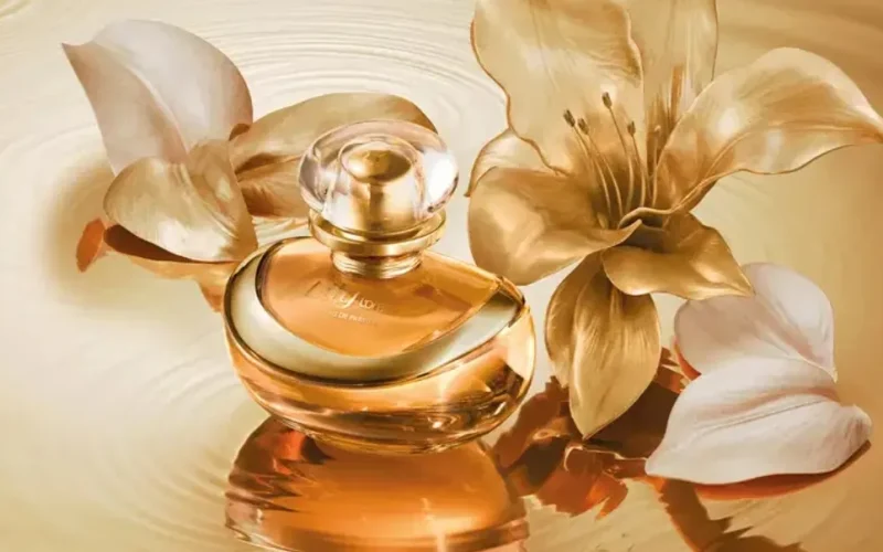 Frasco dourado do perfume Lily L’Or Elixir entre flores de lírio