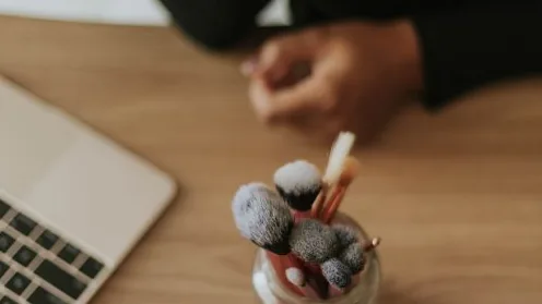 Pincéis de maquiagem sobre uma mesa ao lado de um notebook