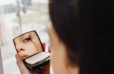 Pessoa aplicando maquiagem nos olhos diante de um espelho compacto