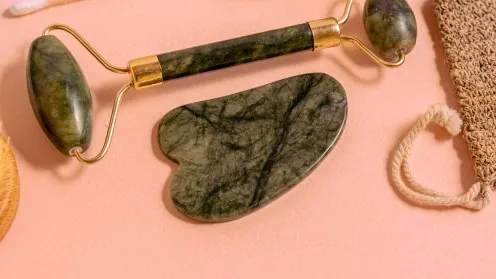 Roller facial e gua sha sobre superfície rosa