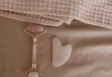 Roller facial e pedra gua sha sobre uma toalha rosa