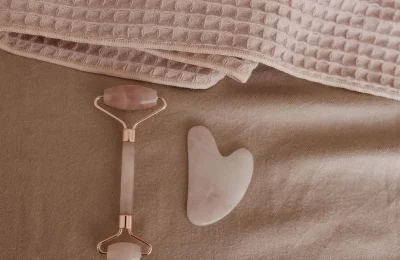 Roller facial e pedra gua sha sobre uma toalha rosa