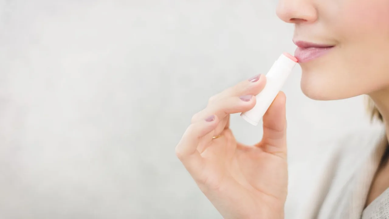Pessoa aplicando produto labial com cor nos lábios.