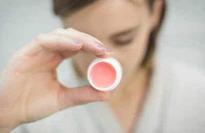 Produto labial com cor em embalagem clara, segurado por uma pessoa.