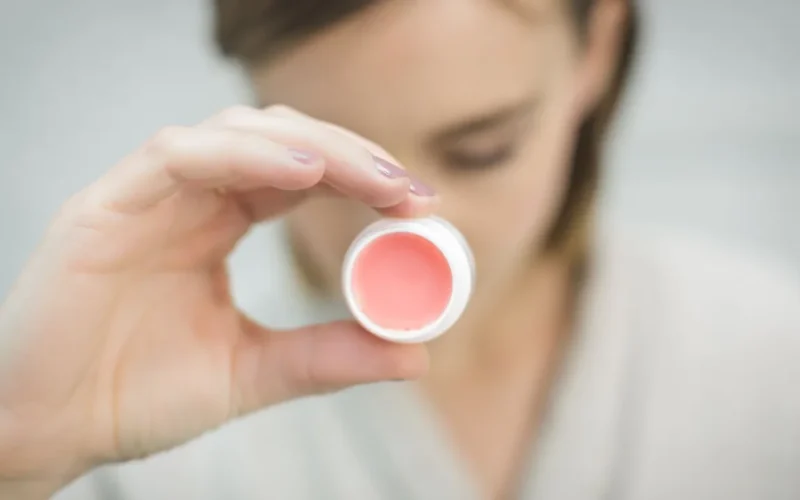 Produto labial com cor em embalagem clara, segurado por uma pessoa.